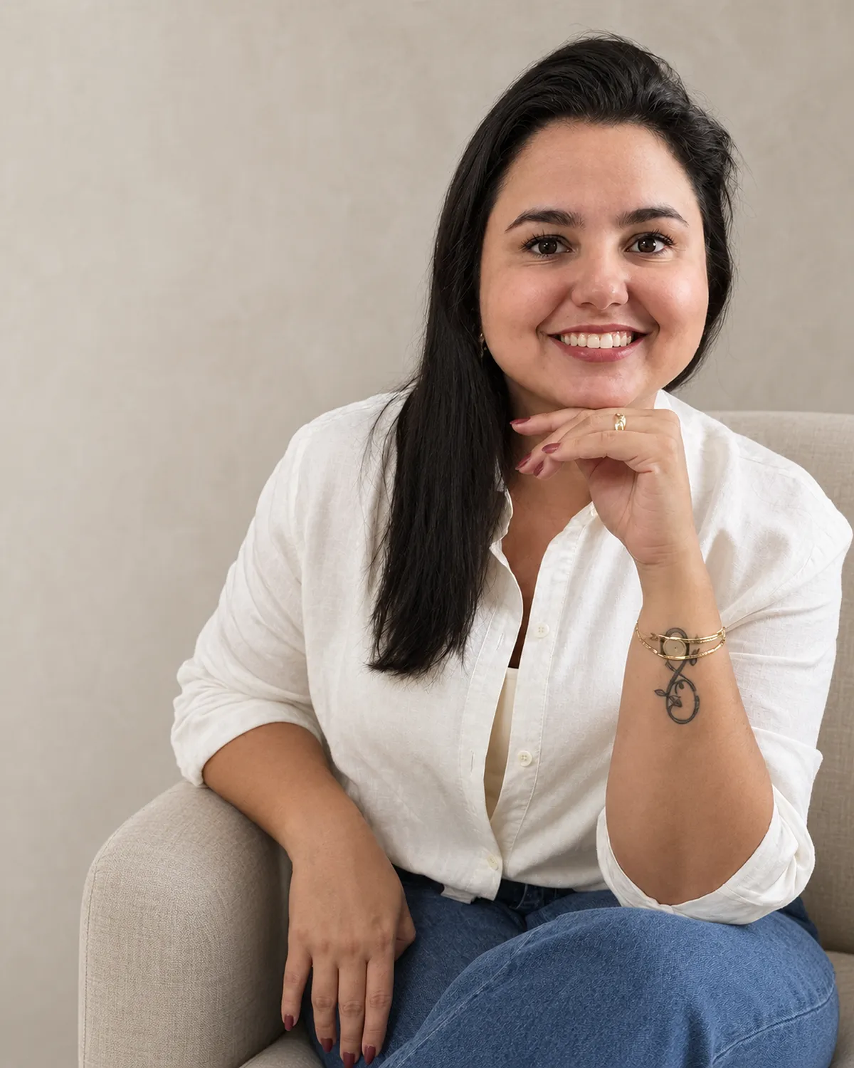 Sabrina Bordon, psicóloga em Campinas, sentada em uma poltrona, apoiando o queixo na mão e sorrindo